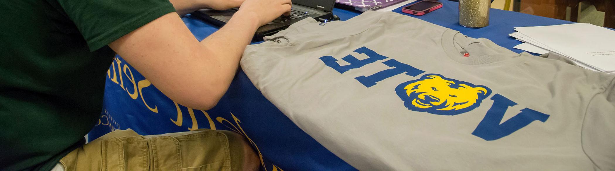 Two students chat at a table where a t-shirt that says 'Bears Vote' on it.