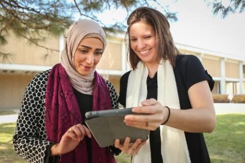 Two female presenting individuals looking together at an iPad outside of Michener library.