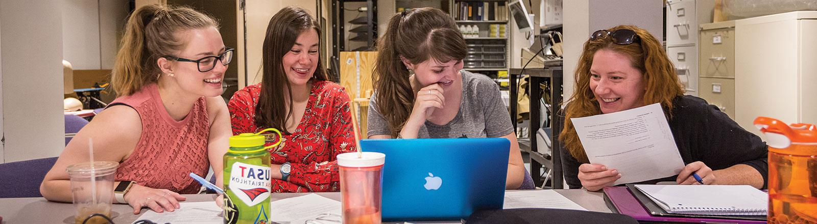 Group of speech pathology students gathered around computer laughing gently