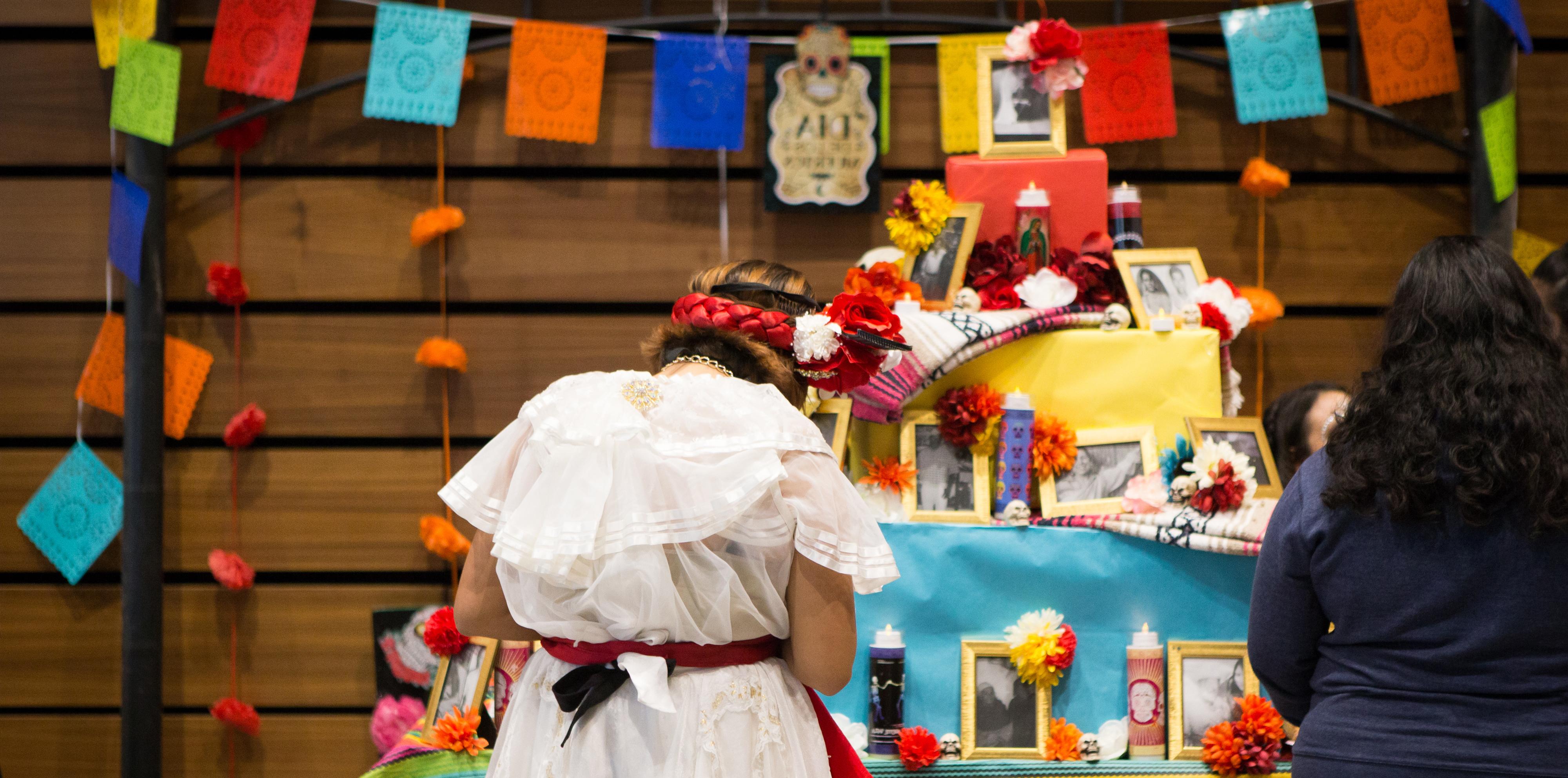 student standing in front of an altar with colorful flags and photographs