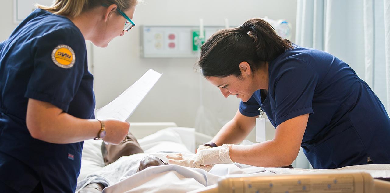 two female nursing students attending to a manikin patient in a bed