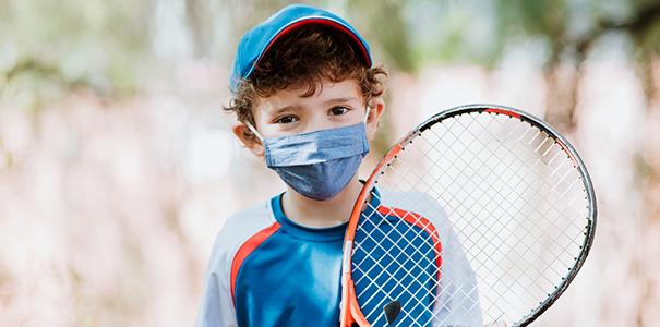 Child with racket and wearing mask